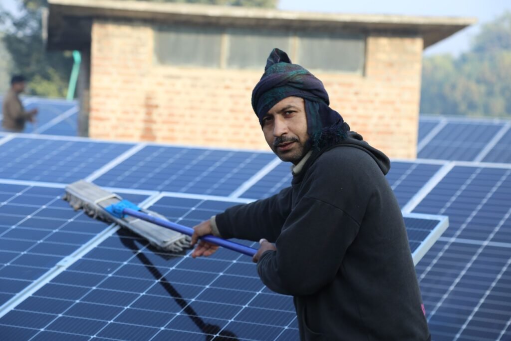 A worker cleaning solar panels with a long-handled mop